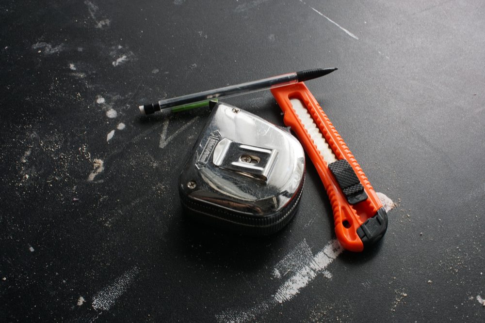 overhead view of a chrome tape measure, lead pencil and a retractable knife