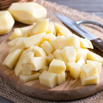 Uncooked cubical yellow potatoes on a chopping board.