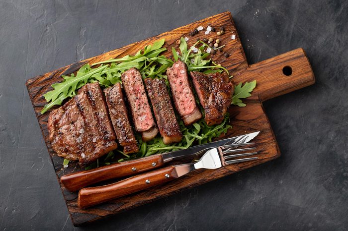 Closeup ready to eat steak new York beef breeds of black Angus with herbs, garlic and butter on a wooden Board. The finished dish for dinner on a dark stone background. Top view