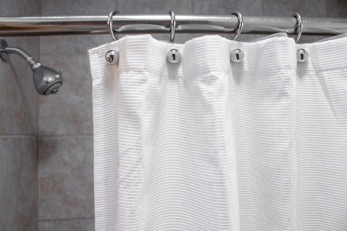 a white shower curtain in an empty shower with water OFF medium shot