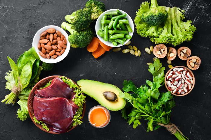 Food containing natural iron. Fe: Liver, avocado, broccoli, spinach, parsley, beans, nuts, on a black stone background. Top view.