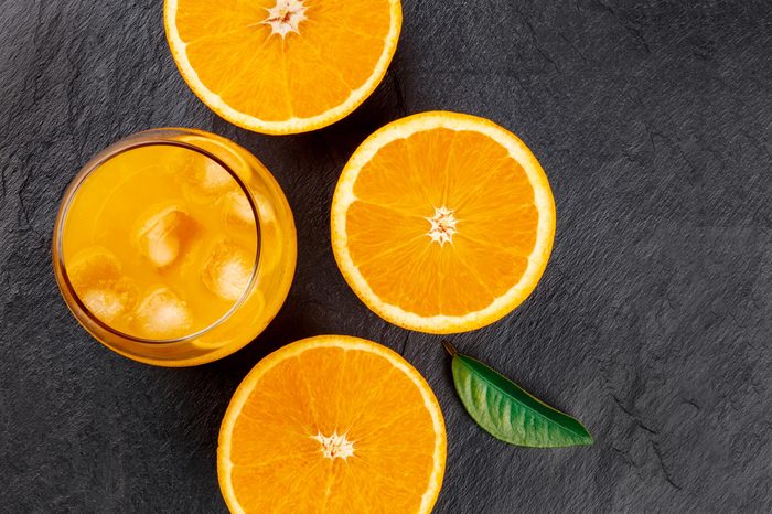 A closeup photo of a glass of fresh orange juice with ice cubes, orange halves and a green leaf, shot from the top on a black background with a place for text