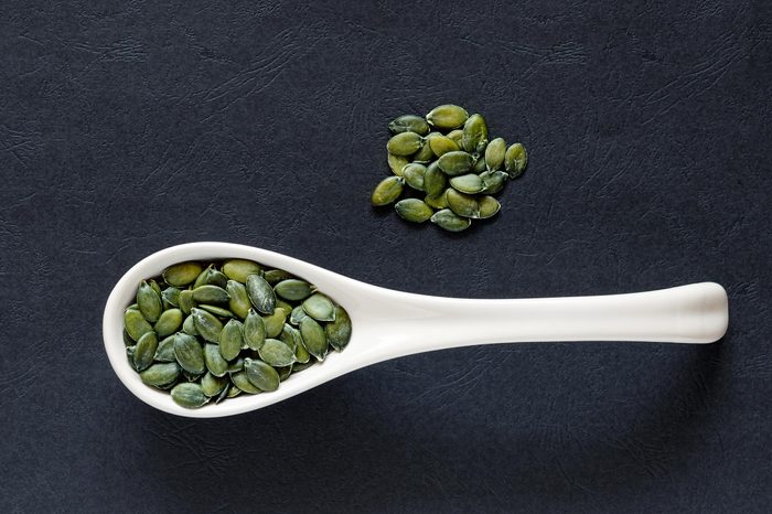 Raw pumpkin seeds in a porcelain spoon an a dark textured background