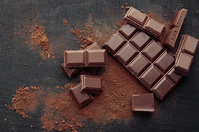 Broken chocolate pieces and cocoa powder on wooden background