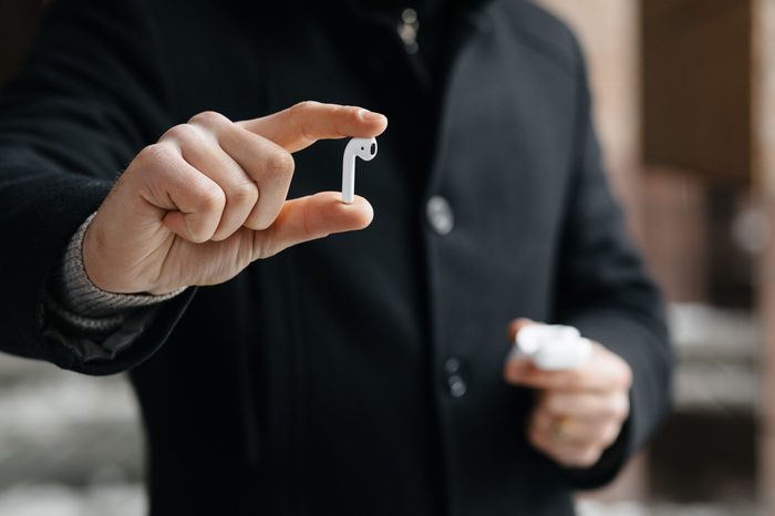 Young man showing wireless headphones on the streets. Man with airpods.