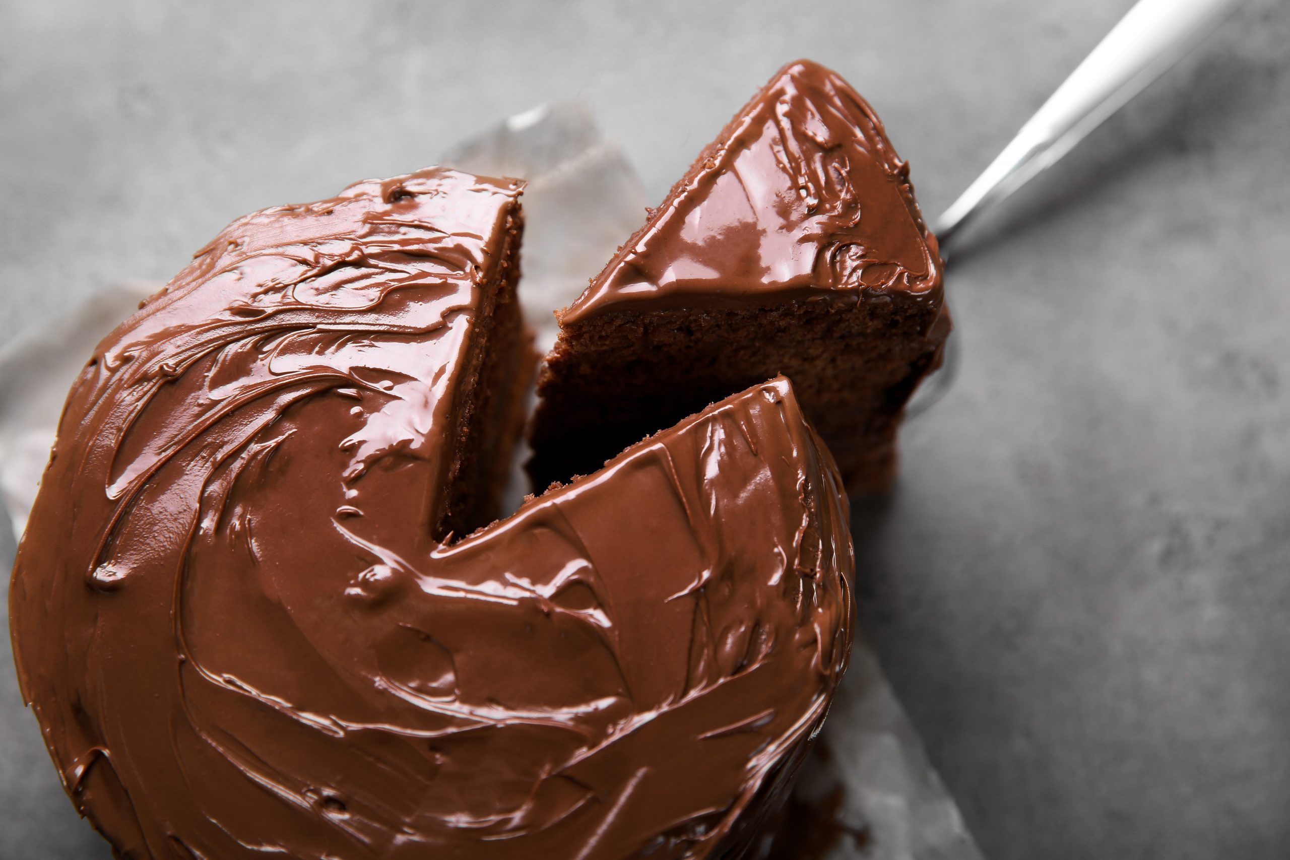 Chocolate cake with a cut piece and blade on gray background, closeup