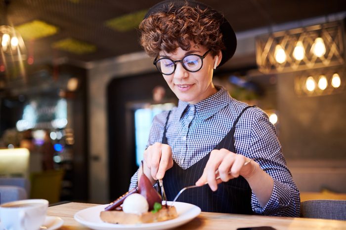 Young woman taking piece of pear dessert off her plate while sitting in cafe at lunch break