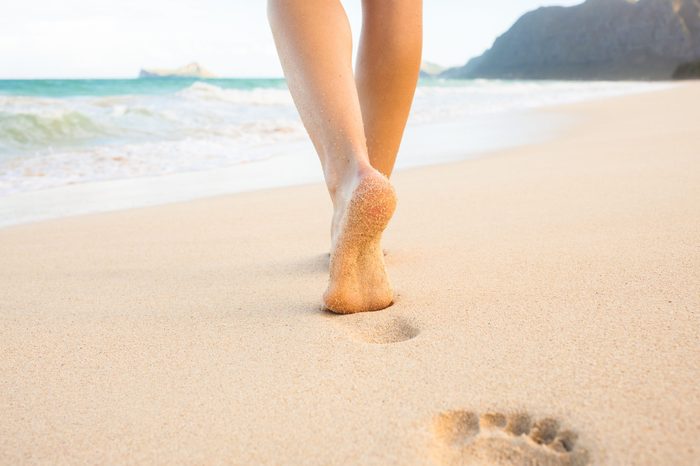 Beach travel - woman walking on sand beach leaving footprints in the sand. Closeup detail of female feet and golden sand on Maui, Hawaii, USA.