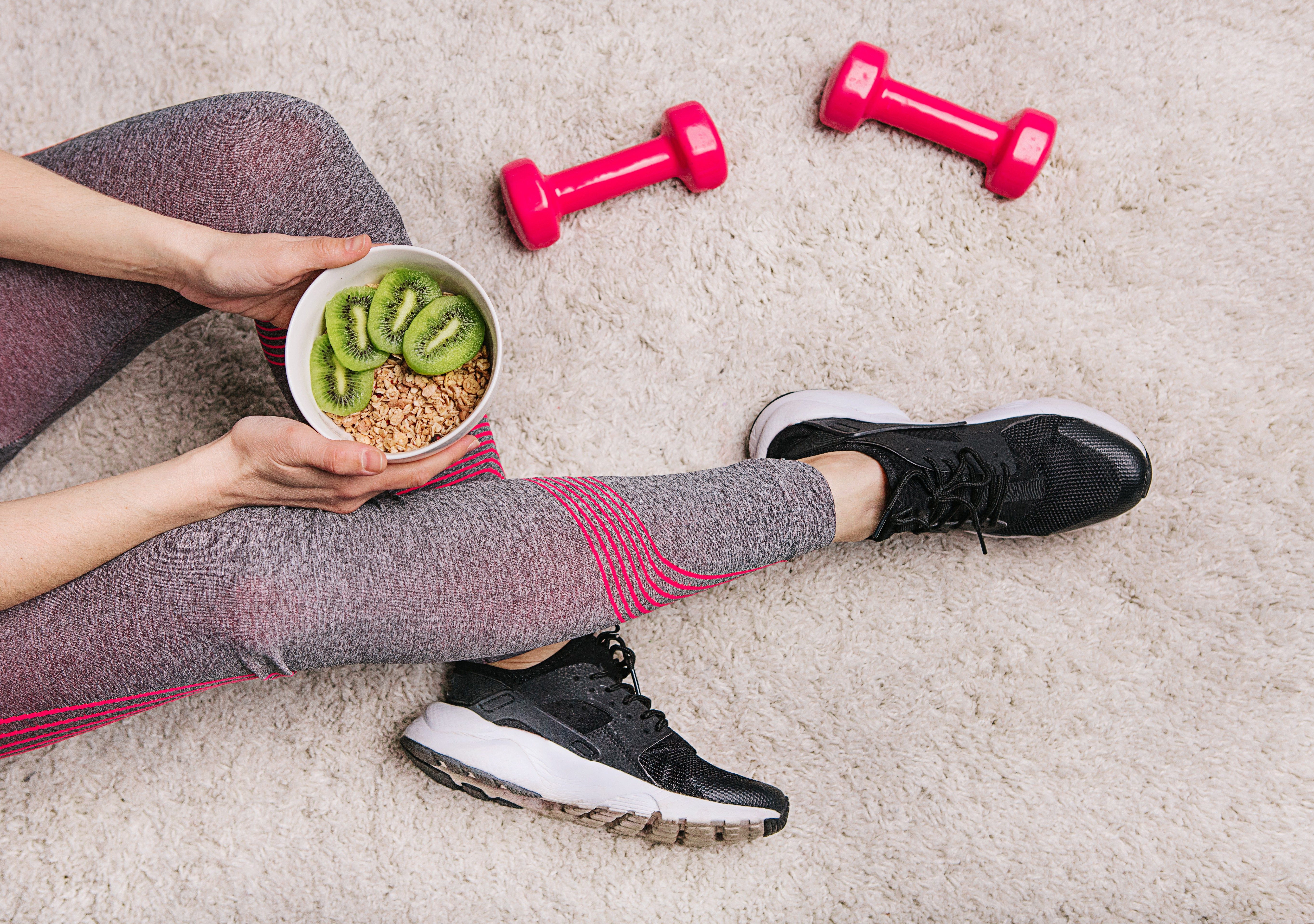 girl in sporting elk holds a plate with muesli and kiwi after fitness workout with dumbbells