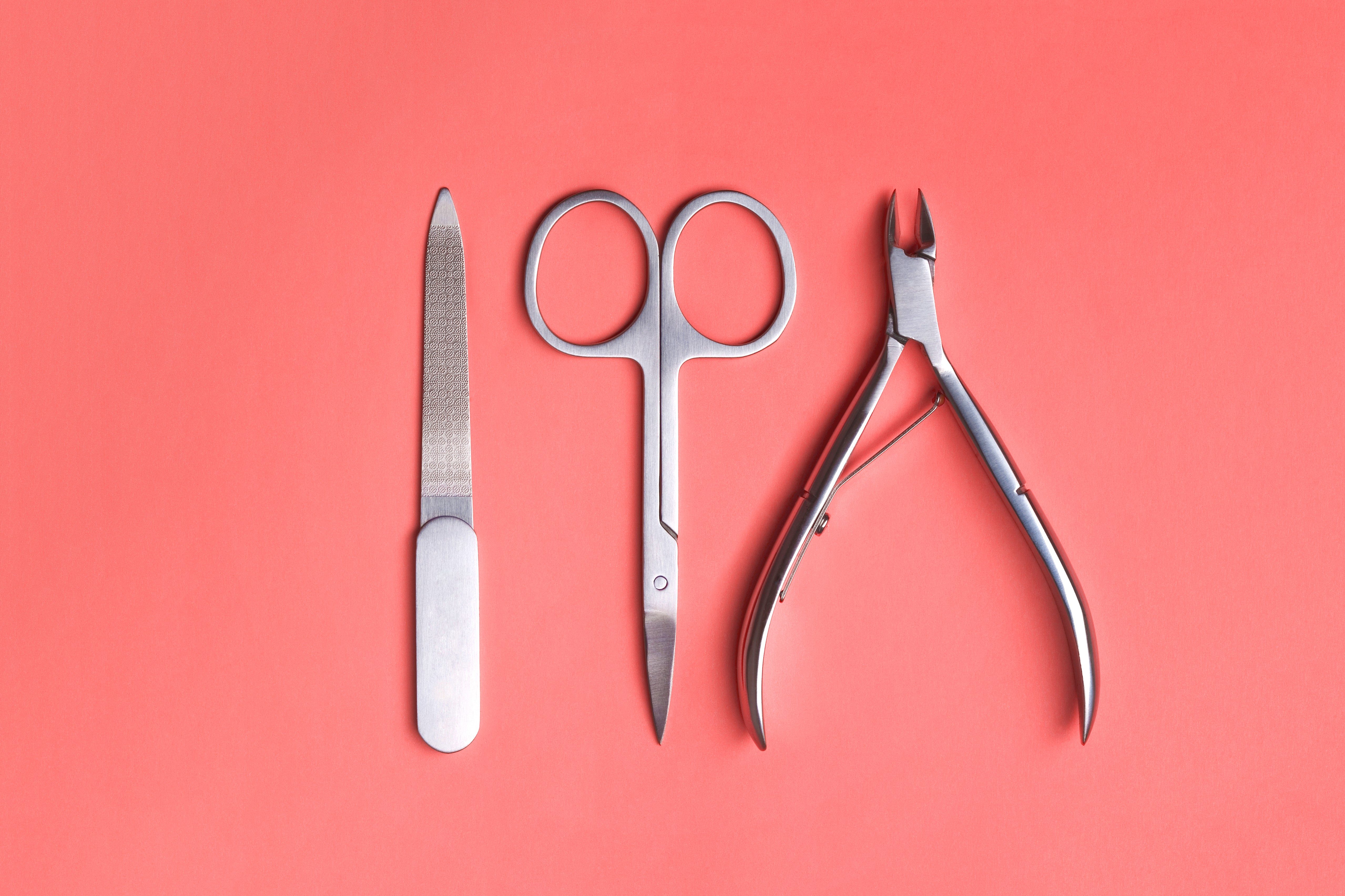 Various elegant manicure tools arranged on Living Coral background. Nail clipper, scissors and file. Color of the year 2019 concept.