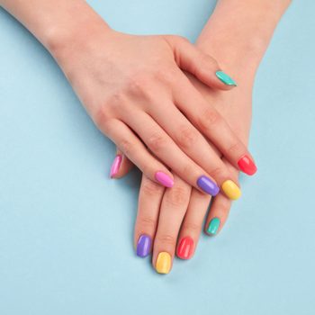 Female beautiful manicured hands. Woman hands with stylish colorful nails on light blue background. Skin and nail care.