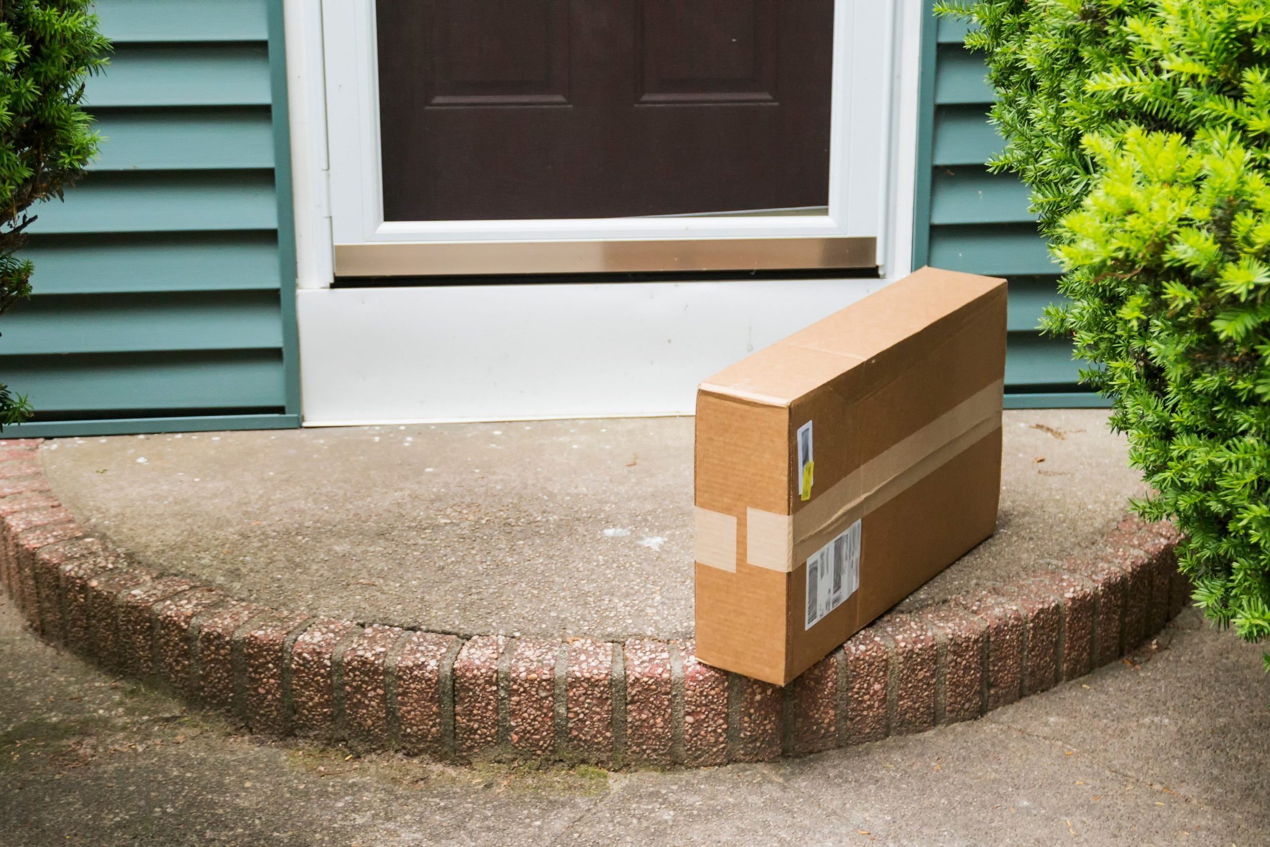 A brown cardboard box is left on the front stoop after being delivered while no one was home.