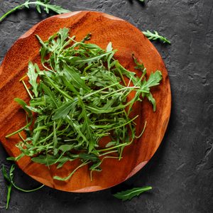 Fresh green arugula leaves in a wooden plate on Dark grey black slate background