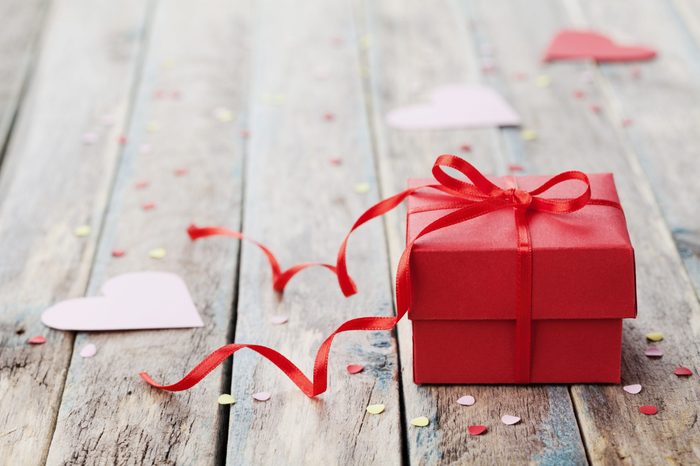 Gift box with red bow ribbon and paper heart on wooden table for Valentines day.