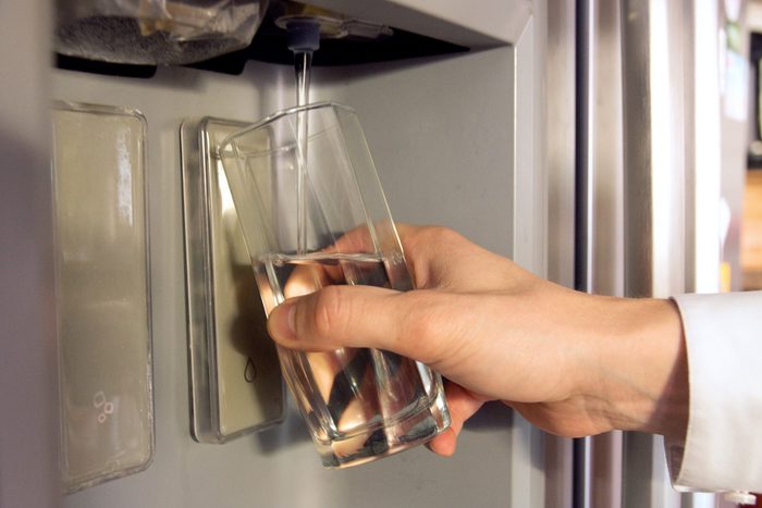 Male hand is pouring cold water from dispenser of home fridge.