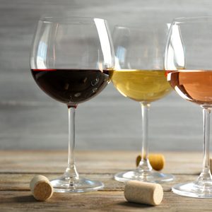Wine glasses in a row and corks on wooden table against grey background