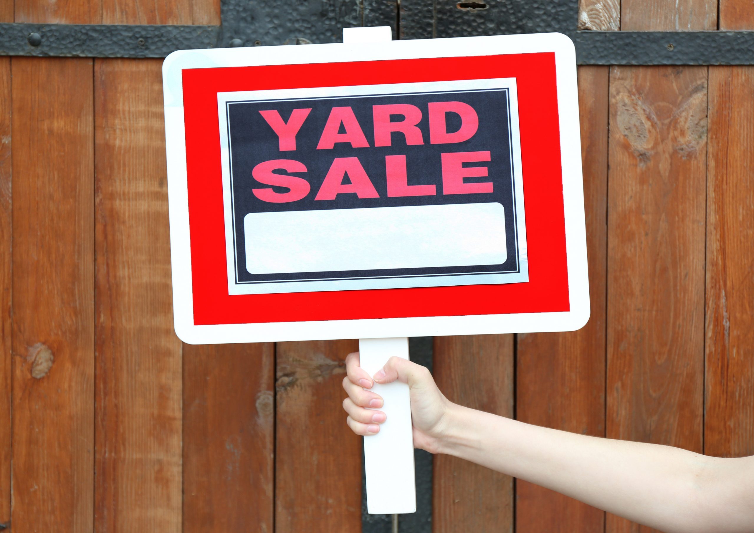 Wooden Yard Sale sign in female hand on wooden fence background