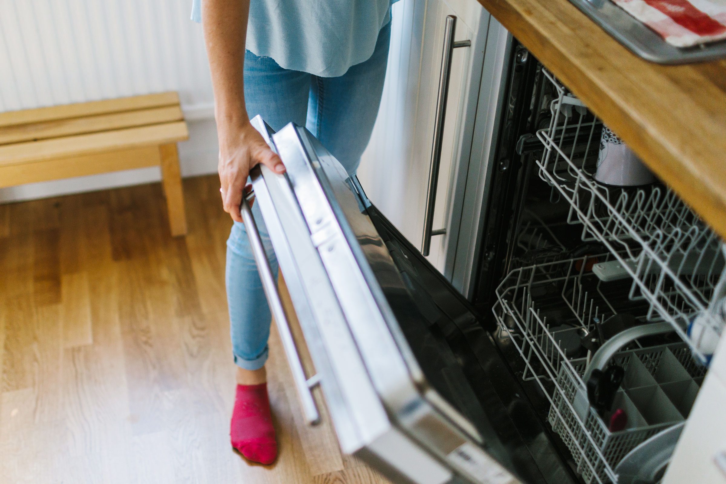 anonymous woman standing in a kitchen opening the dishwasher