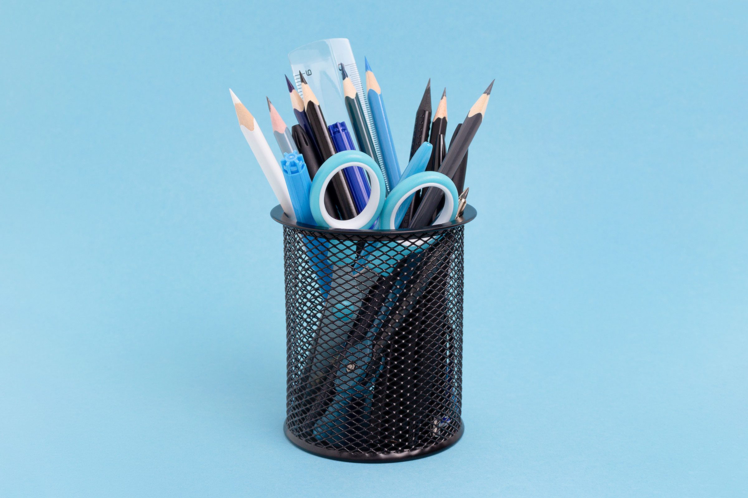 metal pen holder cup with pencils and stationary items on blue background