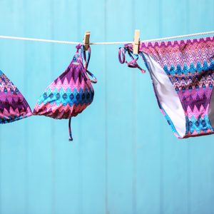 Stylish bikini hanging on rope against color background