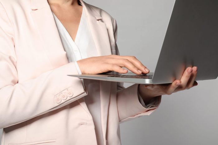 Female manager with laptop on grey background, closeup