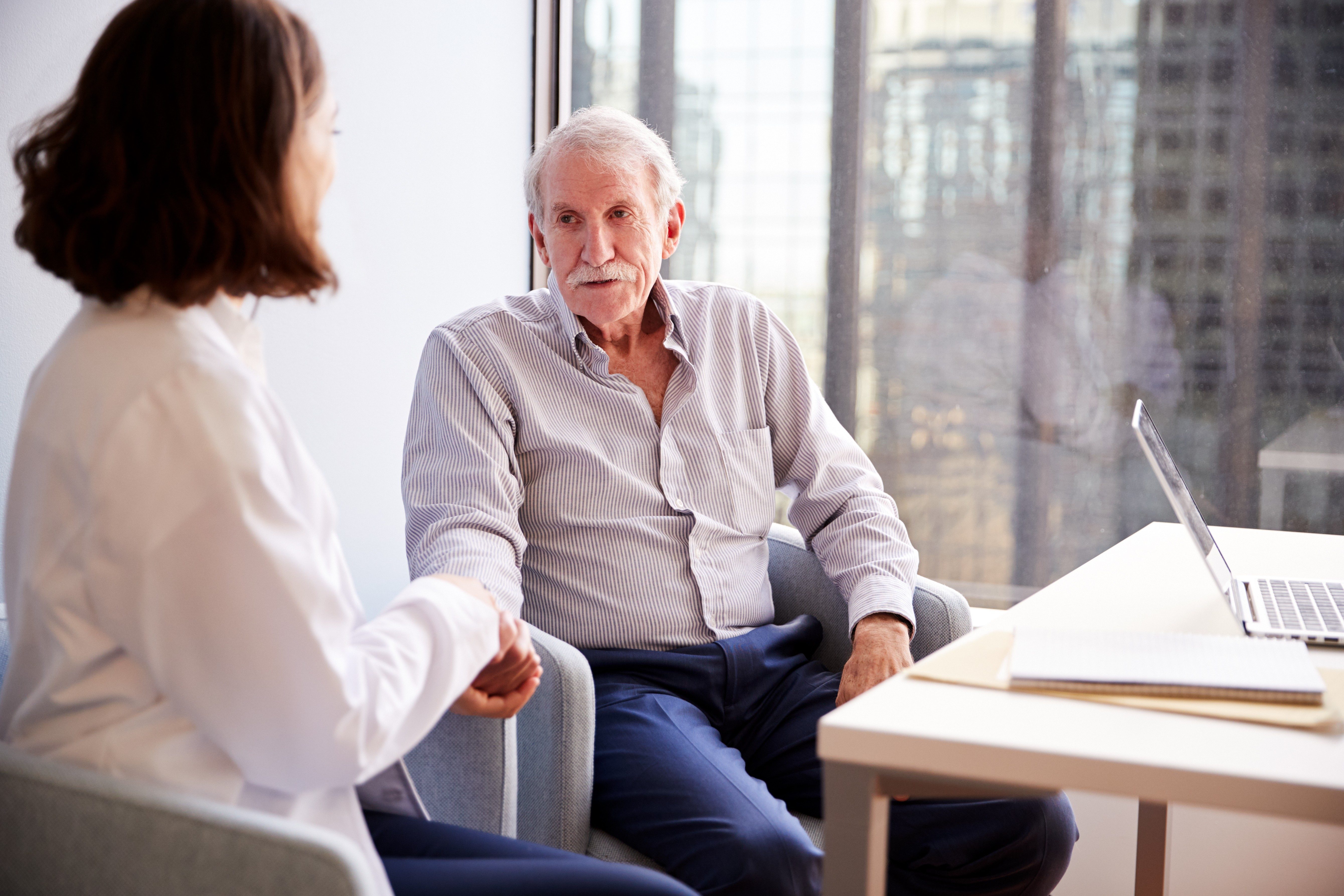 Female Doctor In Office Reassuring Senior Man Patient And Holding His Hands