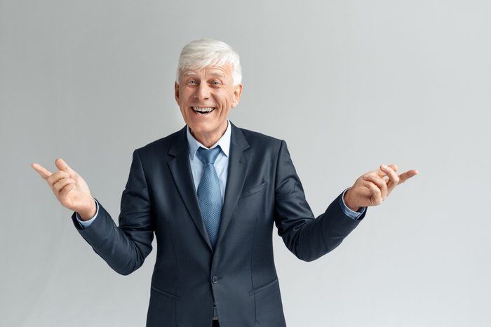 Senior business man studio standing isolated on gray wall hands aside looking camra laughing playful