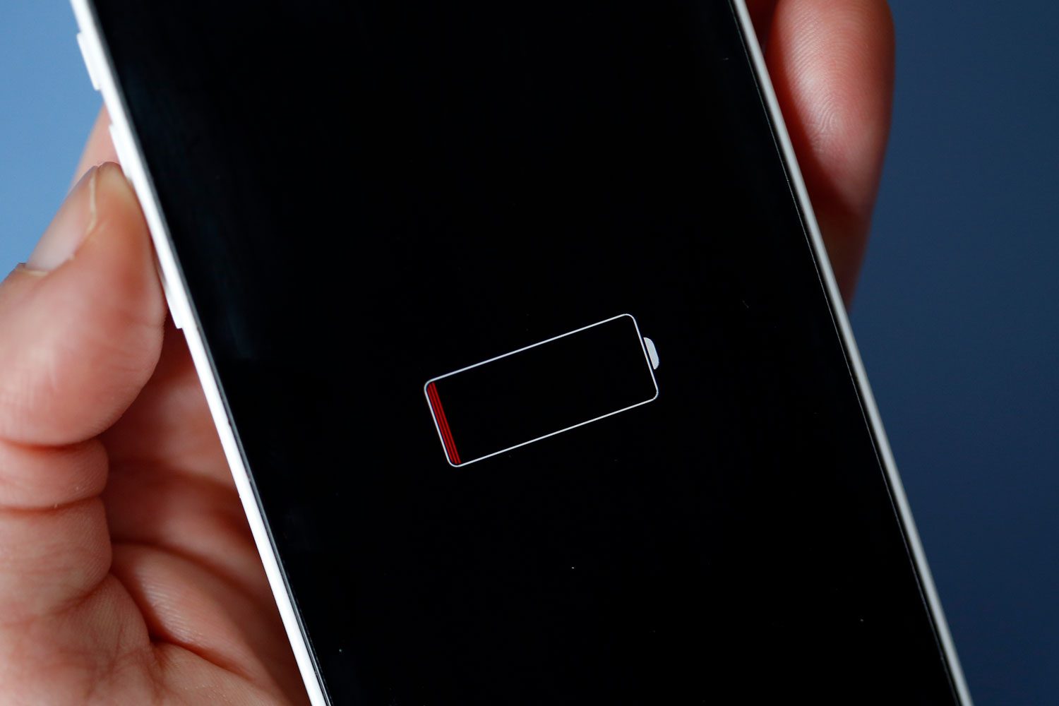 A Woman holds an Apple iPhone on the screen of which we can see a low battery charge indicator