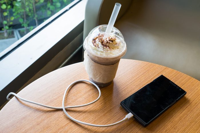 cell phone charging in the cafe with a plastic cup of iced chocolate frappe