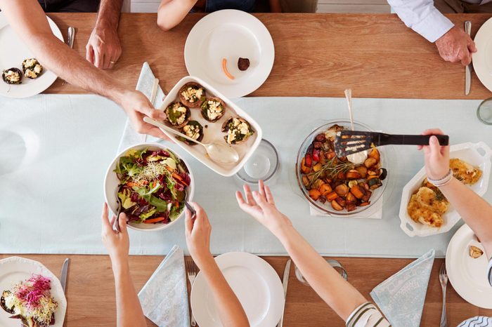 Three generation white family sitting at a dinner table together serving a meal, overhead view