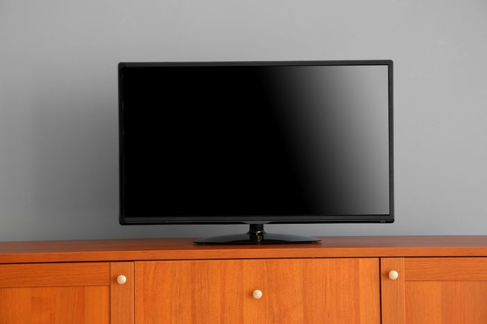 wide screen TV on wooden commode near grey wall