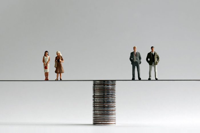 A group of miniature men and women standing on either side of a pile of coins.