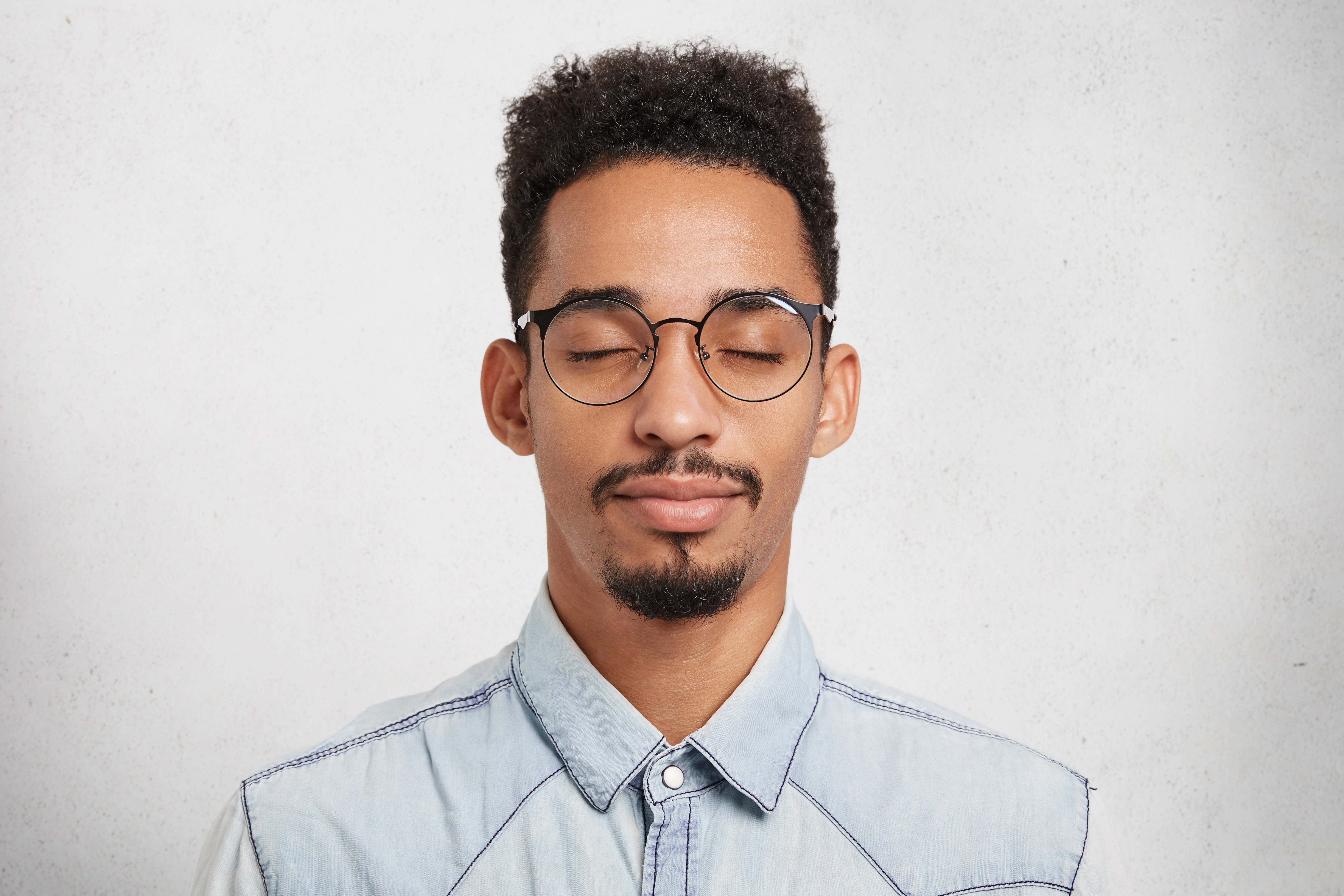 Busy male enterpreneur closes eyes, tries to concentrate, being fatigue after hard work, wants to sleep. Focused male with closed eyes, mustache and beard imagines something pleasant and unforgettable