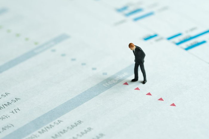 Miniature businessman looking at red down arrows of investment report, stock price drop, negative sentiment, financial crisis, situations in which some financial assets suddenly lose or value drop.