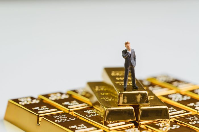 Success miniature rich businessman standing on stack of gold bar, bullion or ingot using as wealth management, gold investment and financial asset.