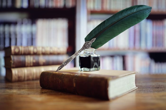 Quill pen and ink well resting on an old book in a library concept for literature, writing, author and history