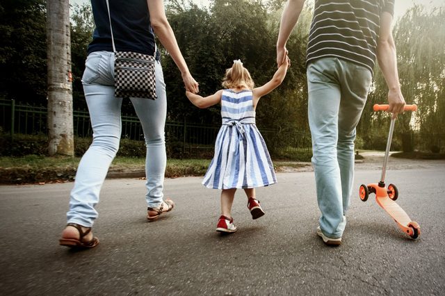 happy stylish parents holding hands with daughter and walking in sunny  street, amazing family moment. father's mother's day