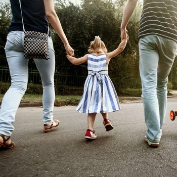 happy stylish parents holding hands with daughter and walking in sunny  street, amazing family moment. father's mother's day