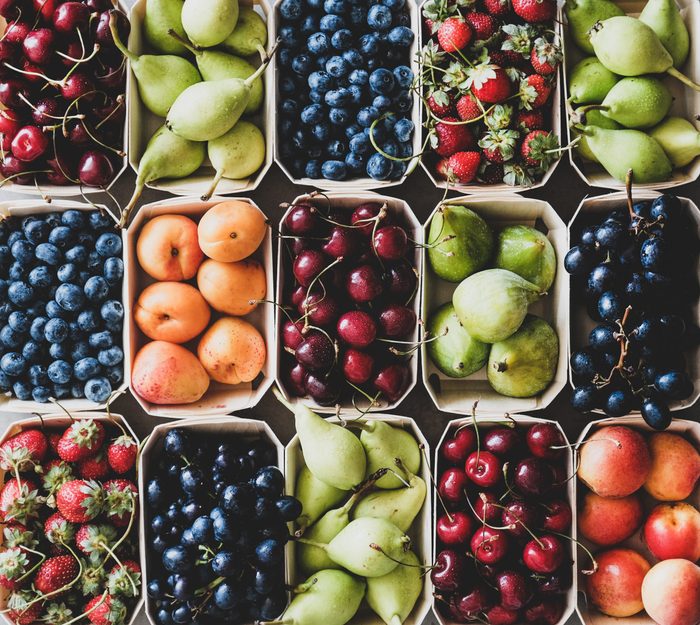 Summer fruit and berry assortment. Flat-lay of strawberries, cherries, grapes, blueberries, pears, apricots, figs in eco-friendly boxes over grey background, top view, close-up. Local farmers produce