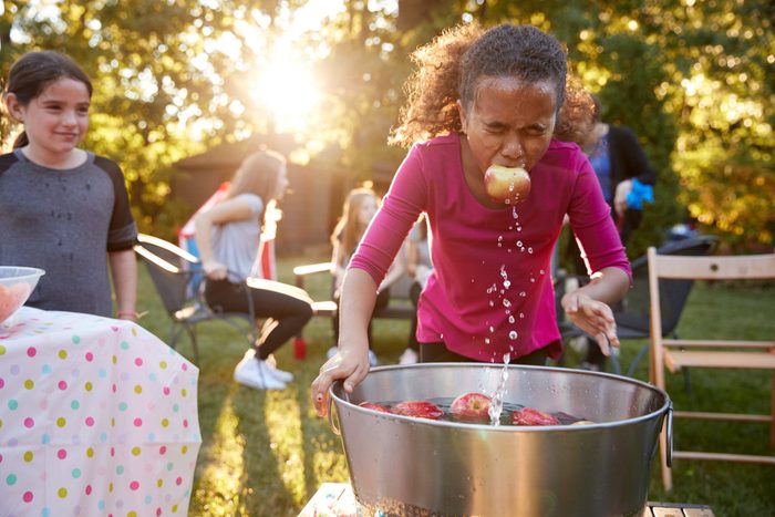 Pre-teen girl, apple in mouth, apple bobbing at garden party