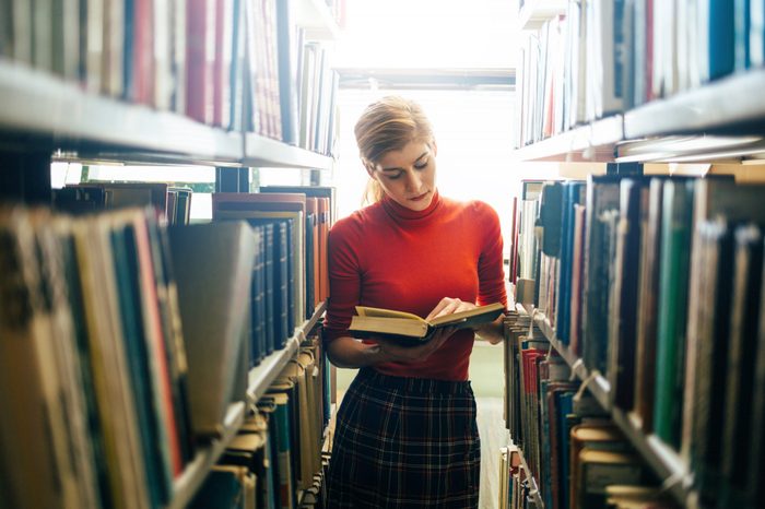 Woman reading a book in library. Portrait of college girl reading book in library