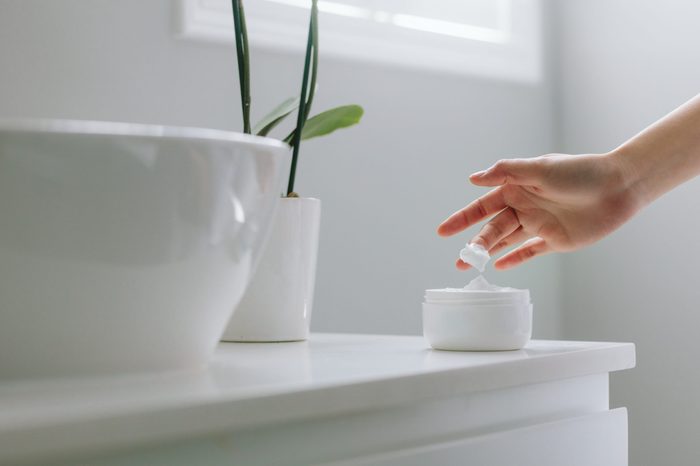 Close up of female hands taking moisturizing cream from bottle in bathroom. Woman taking care of her dry complexion.