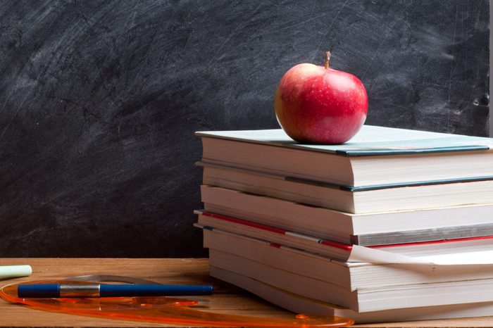 red apple resting on the book with chalk board as background