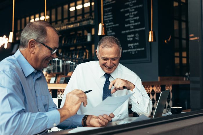 Happy senior business people talking over few reports at cafe. Two business partners reviewing contract papers at a restaurant.