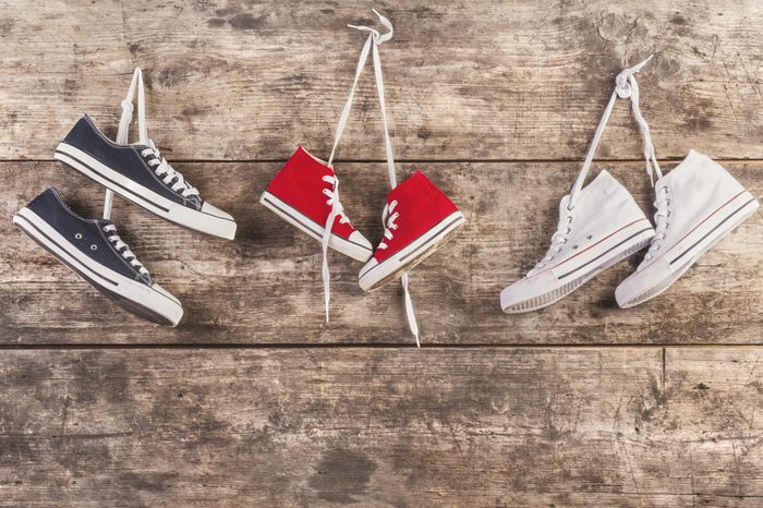 Three pairs of sports shoes hang on a nail on a wooden fence background