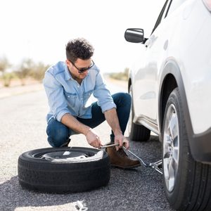 Handsome young man lifting the car on the jack for changing flat tire on the road