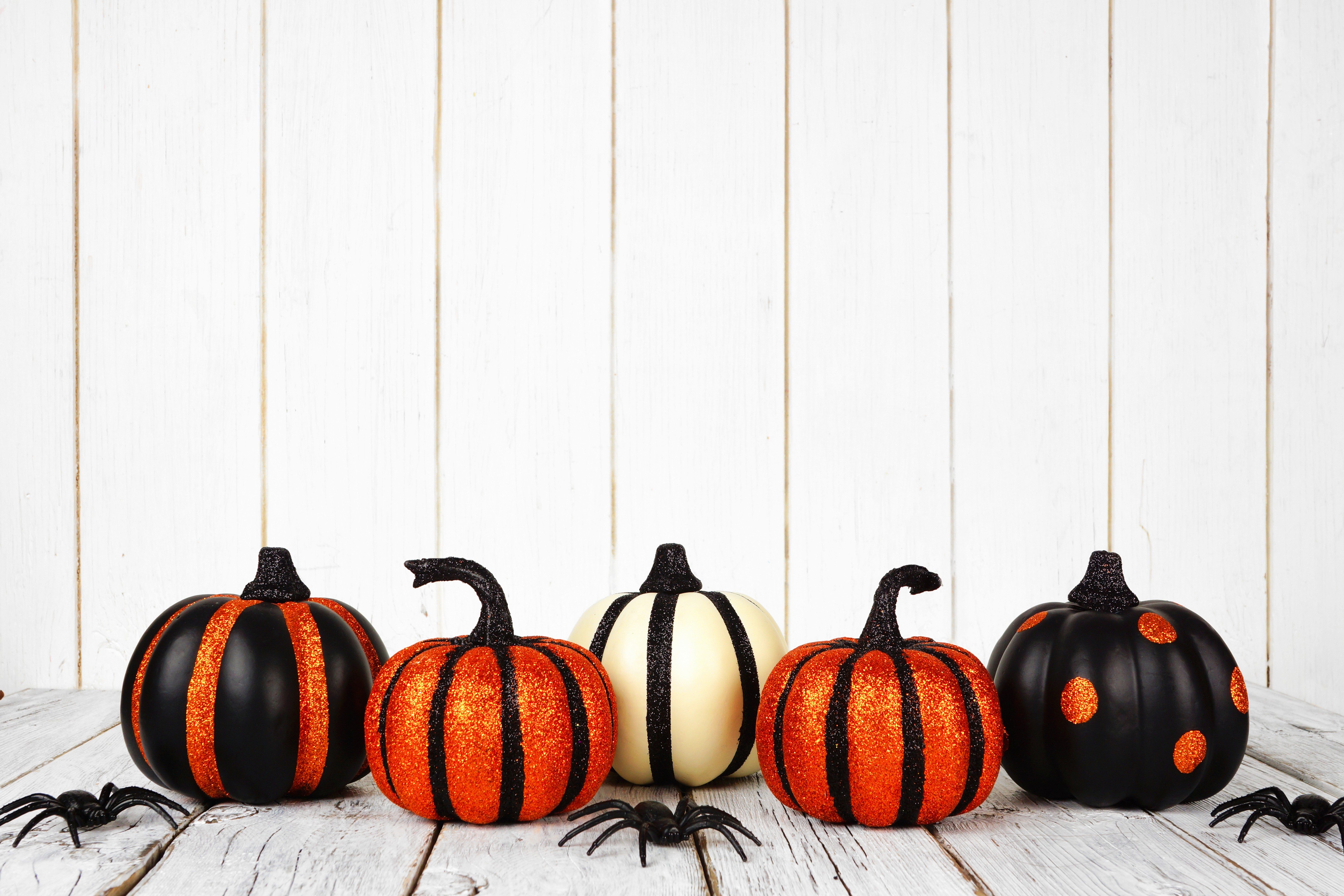 Black and orange glittery Halloween pumpkins against a white wood background