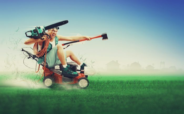 Crazy workman covered with instruments driving lawn mower over green grass
