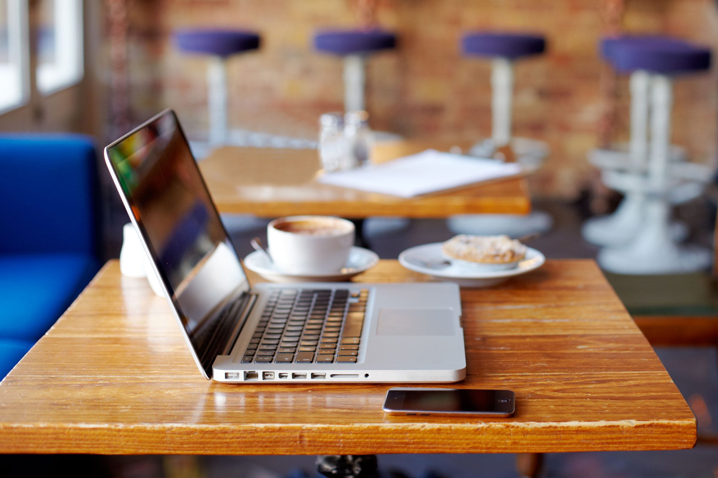 a laptop, a smartphone, a coffee, and a pastry sit on a table at a cafe with free open wifi