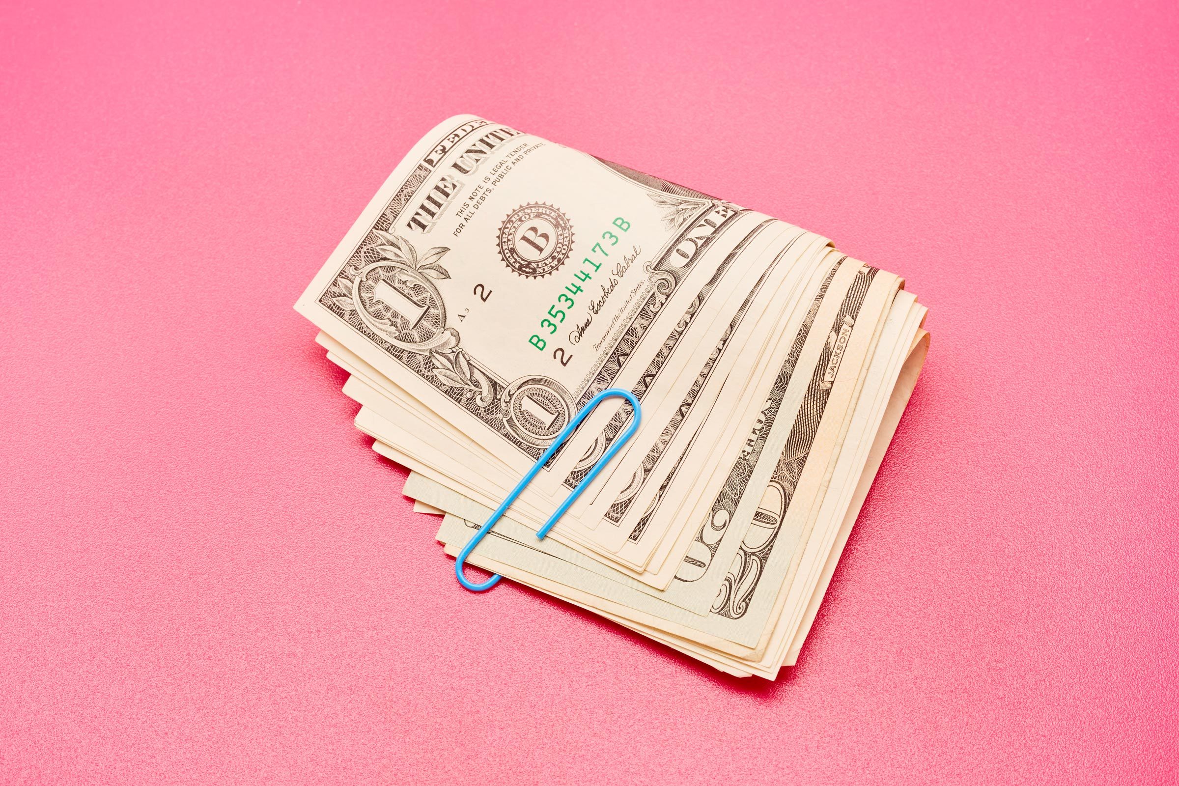 stack on money in paper clip on pink background